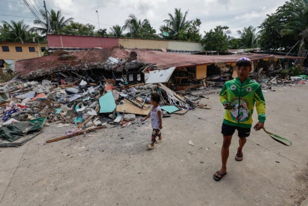 Residents on Friday walk past collapsed houses in a community of typhoon survivors that was affected by an earthquake in Bogo City, Cebu, Philippines, on Tuesday. On Friday, a typhoon struck the northern part of the nation. Photo by Rolex Dela Pena/EPA